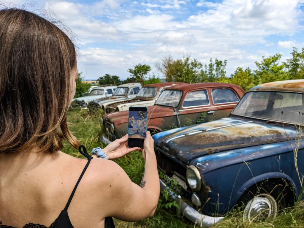 jong meisje kijkt naar verlaten oude auto's met een urbex kaart op een telefoon